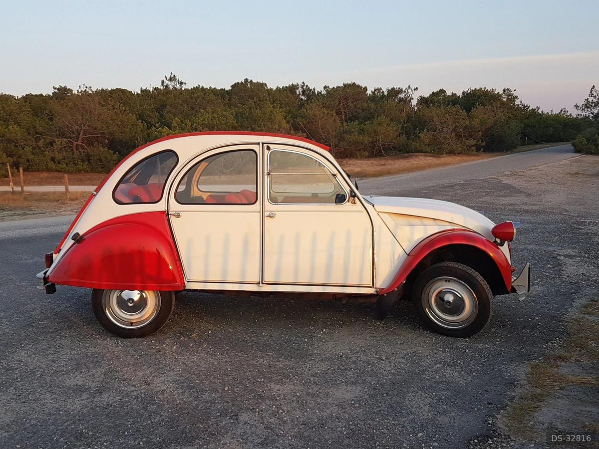 Cream and red Citroën 2CV parked on an empty rural road at dusk