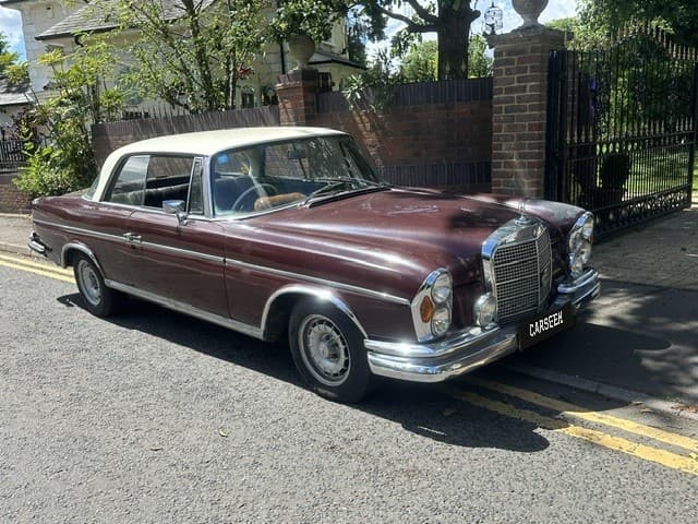Burgundy 1960s Mercedes-Benz coupé with cream roof parked beside brick gate pillars
