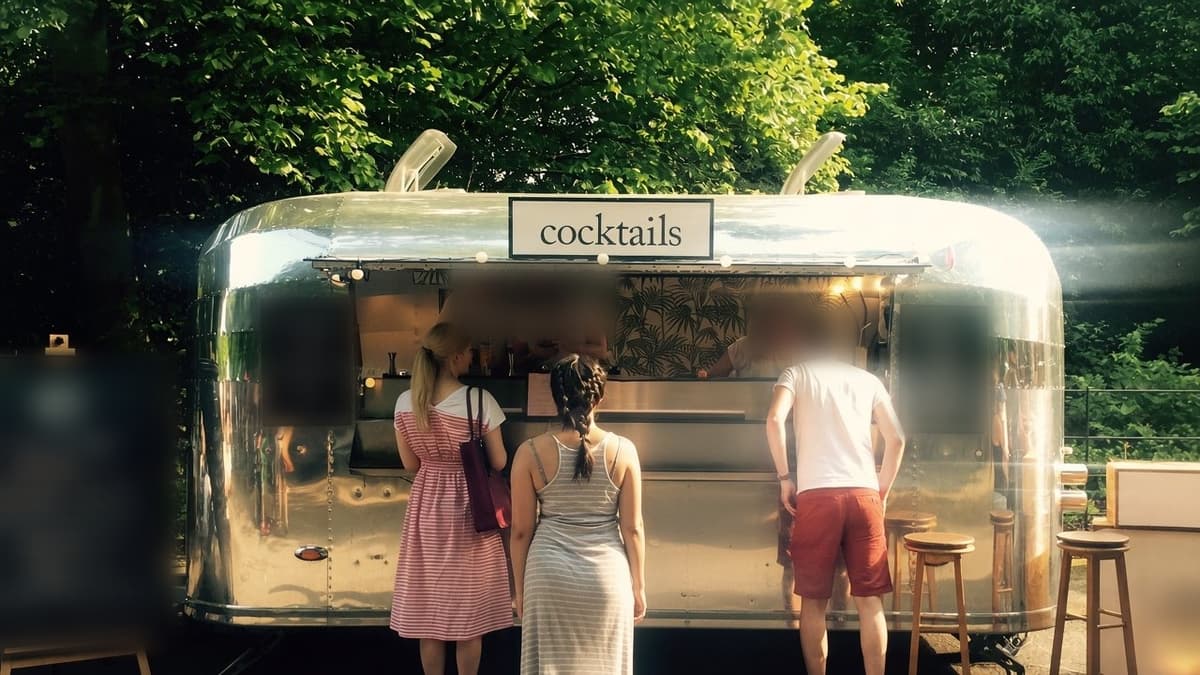 Polished aluminium cocktail bar trailer with serving hatch open among trees