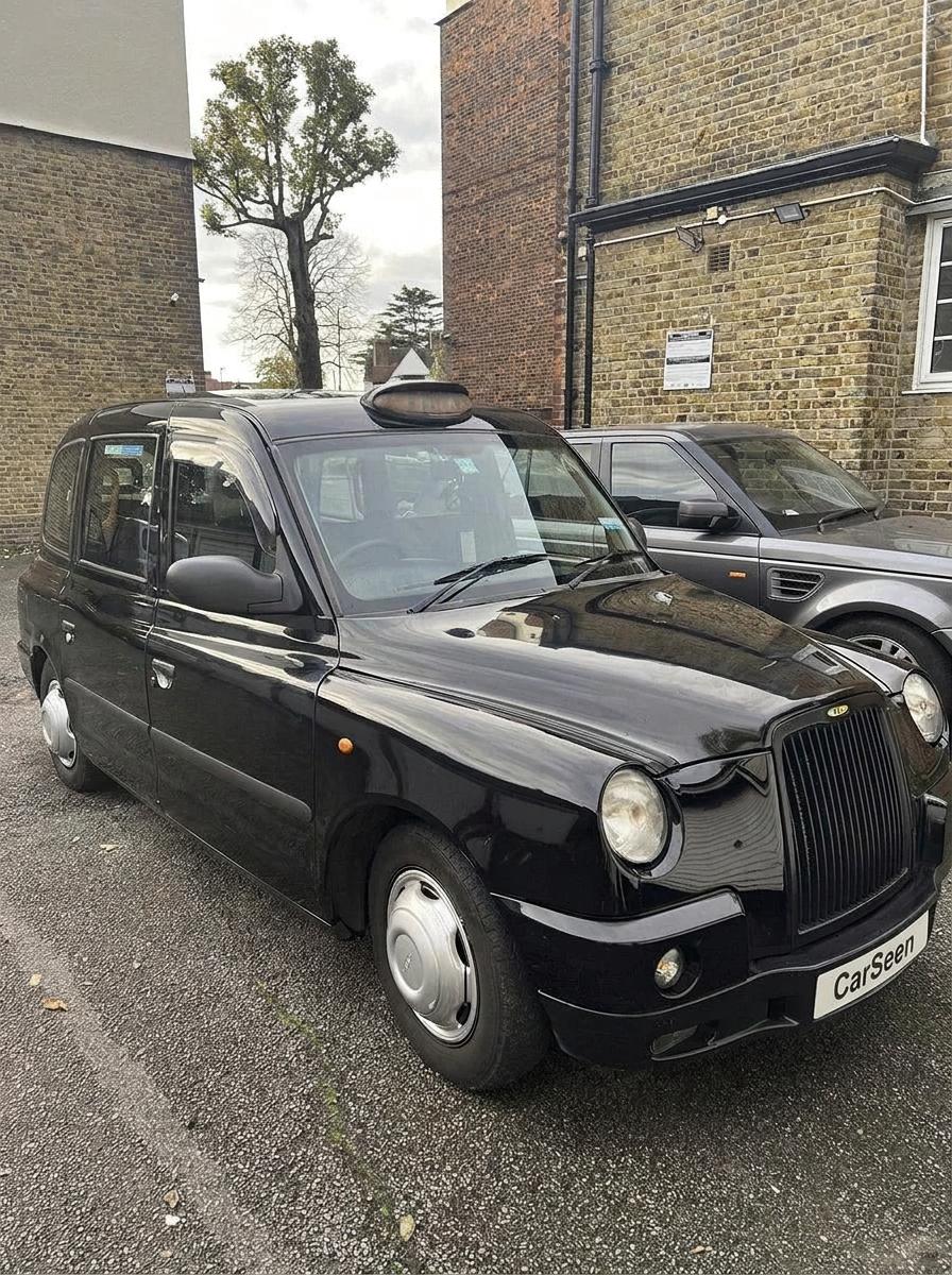 Black London taxi parked beside a brick building