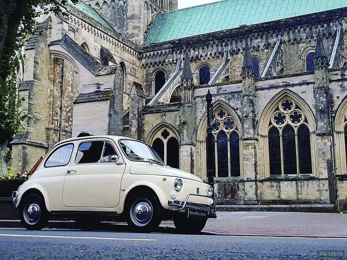 Cream Fiat 500 L parked below a gothic cathedral