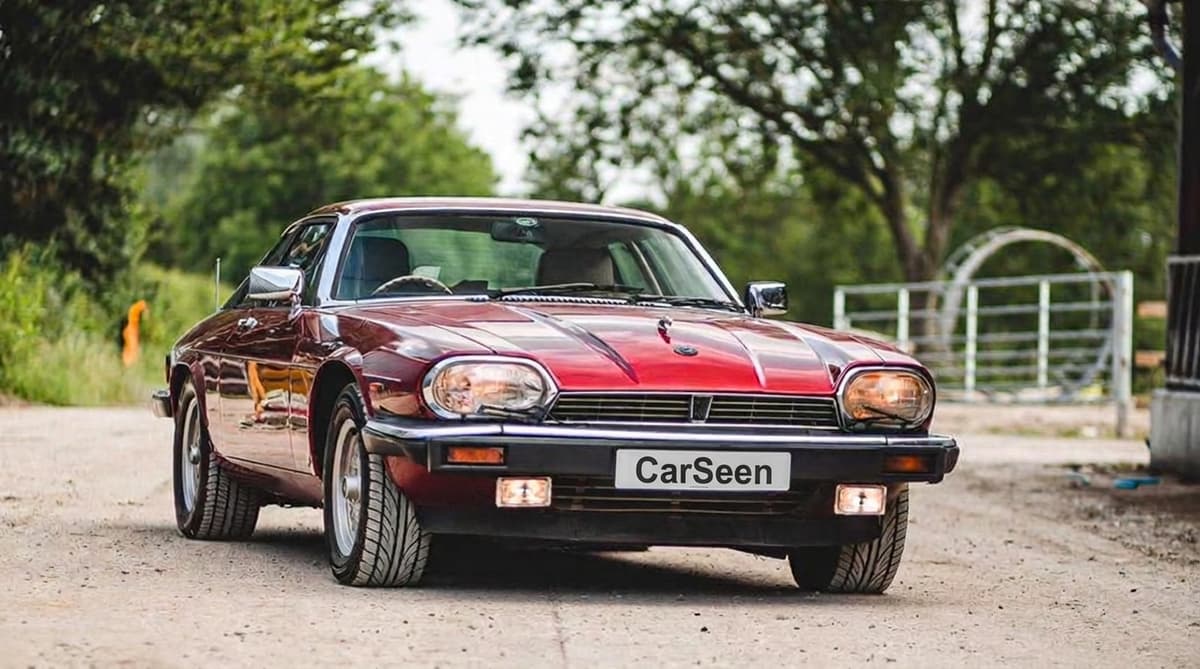 Claret Jaguar XJS coupe angled on a gravel track lined with trees