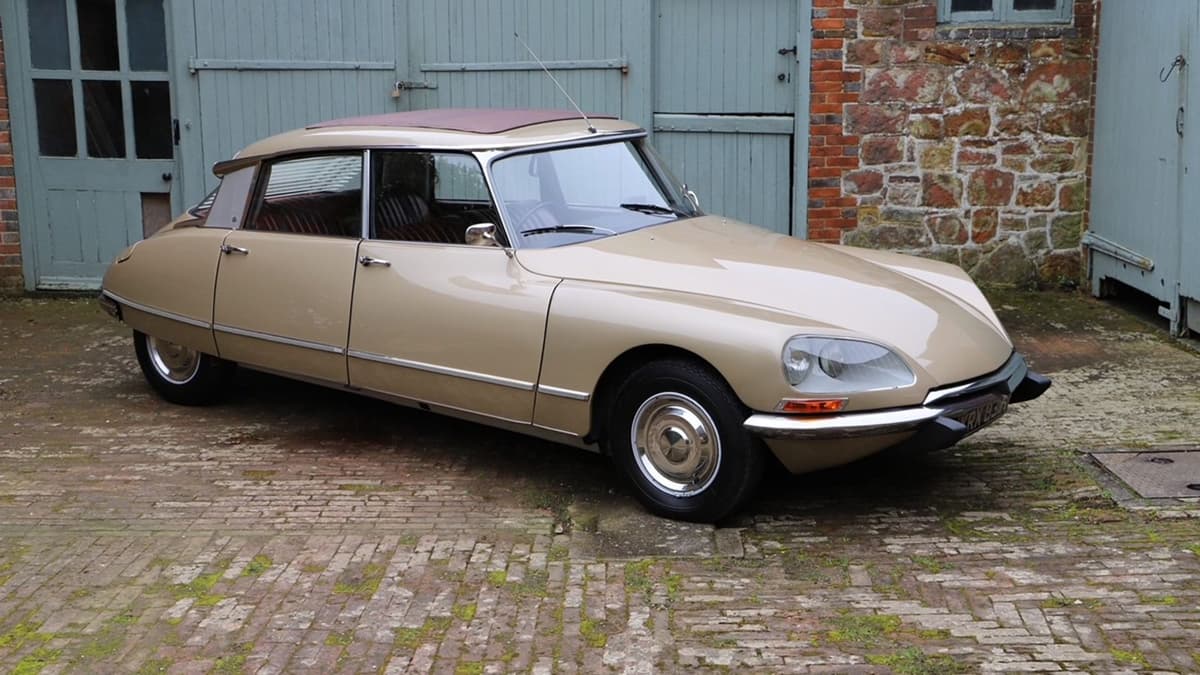 Beige Citroën DS21 with a maroon roof on brick paving outside a stone workshop