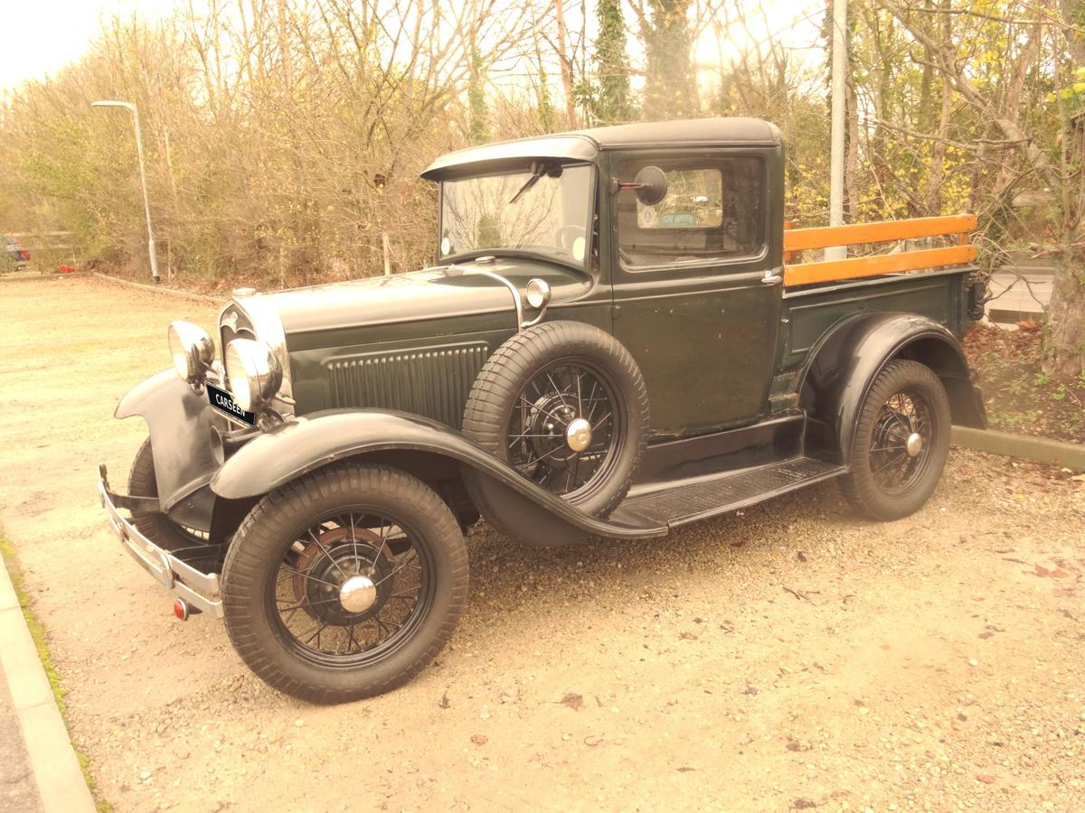 1931 Ford Model A pickup in green with black wings, side profile with wooden stake sides, on a gravel drive