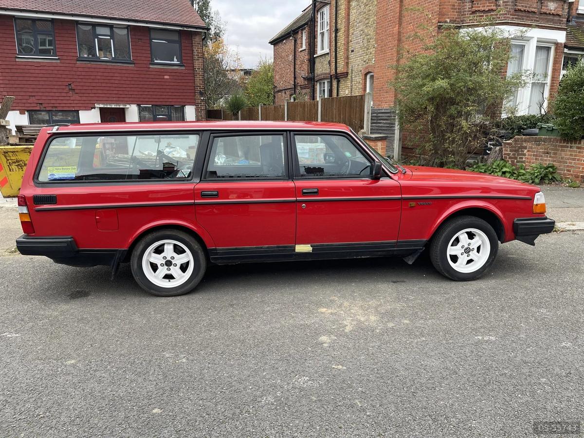 Red Volvo 240 estate with white wheels on a residential street