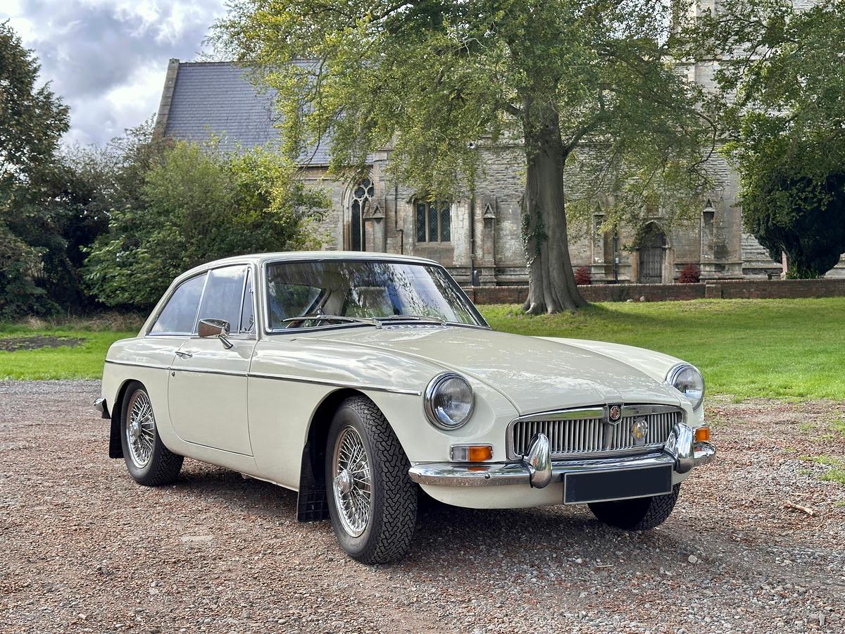 Old English White 1968 MG B GT on wire wheels in front of a stone church